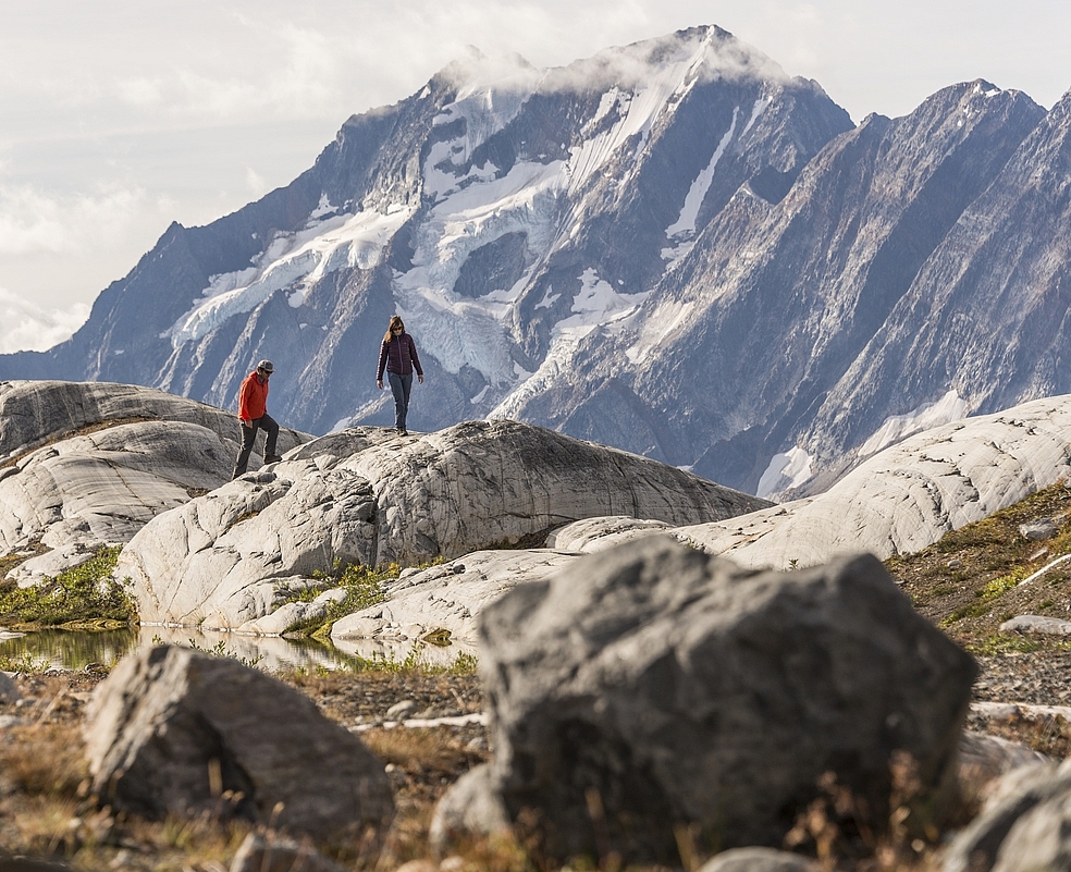 Two hikers at the top of a rock face with a huge mountain in the distance.