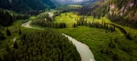 A river runs through a verdant green valley with misty mountains in the distance.